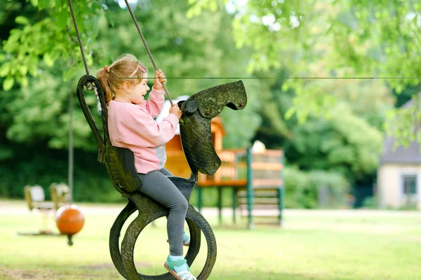 Szczęśliwa mała przedszkolanka bawiąca się na huśtawce w ogrodzie. Zdrowe dziecko huśtawka w letni dzień. Dzieci ćwiczą na świeżym powietrzu, uśmiechnięte dziecko się śmieje. Stare opony jak huśtawka. — Zdjęcie stockowe