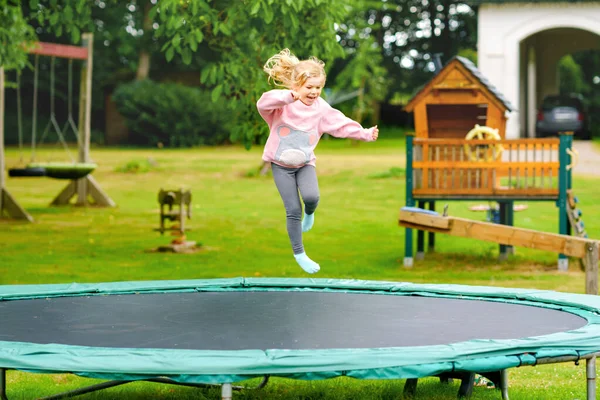 Uma miúda pré-escolar a saltar em trampolim. Criança engraçada feliz se divertindo com a atividade ao ar livre no verão. Esportes e exercícios para crianças. — Fotografia de Stock