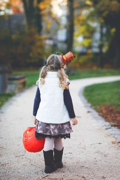 Cadılar Bayramı 'nda cadı kılığına girmiş küçük bir kız. Mutlu çocuk dışarıda, turuncu komik şapkası ve tatlı lanetli balkabağı çantasıyla. Ekim 'de aile mevsimi. Tanımlanamayan yüz — Stok fotoğraf