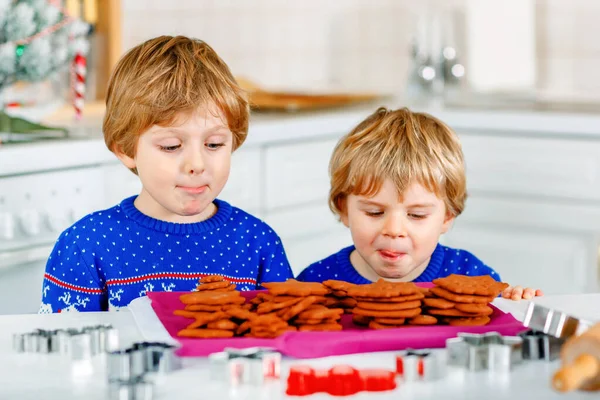 Dva malí předškoláci pečou perníkové sušenky. Šťastní sourozenci, děti ve vánočních svetrech. Kuchyně vyzdobená na Vánoce. Bratři bojují, dělají zmatek. Vánoční rodinná činnost — Stock fotografie