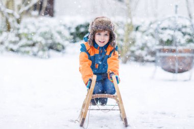 Küçük çocuk kar yağışı sırasında kızak sürmekten hoşlanıyor. Eski model kızakla gezen mutlu anaokulu çocuğu. Çocuk dışarıda karla oynuyor. Kışın aile Noel tatili için aktif eğlence