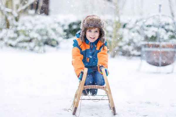 Küçük çocuk kar yağışı sırasında kızak sürmekten hoşlanıyor. Eski model kızakla gezen mutlu anaokulu çocuğu. Çocuk dışarıda karla oynuyor. Kışın aile Noel tatili için aktif eğlence — Stok fotoğraf