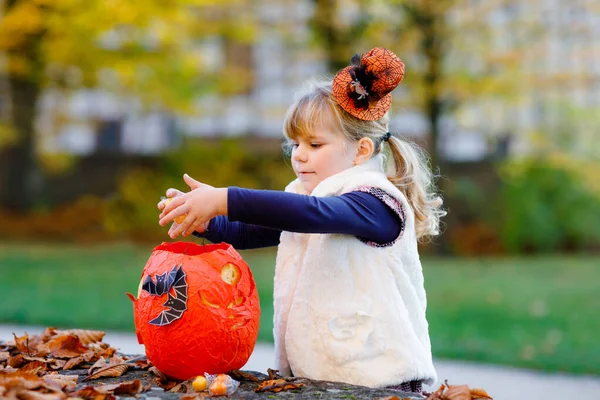 Petite fille tout-petit habillée comme un tour de sorcière ou de traiter à Halloween. Joyeux enfant à l'extérieur, avec chapeau orange drôle et sac de citrouille pour hanter doux. Saison des festivals familiaux en octobre. Activité de plein air — Photo