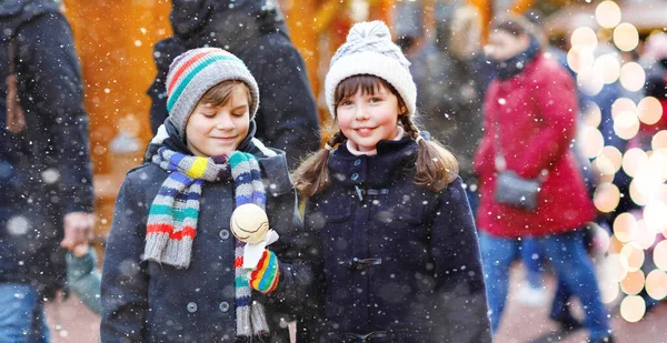 Little cute kid girl and boy eating white chocolate covered strawberries and apple on skewer on traditional German Christmas market. Happy children, best friends, twins and siblings on snowy day — Stock Photo, Image