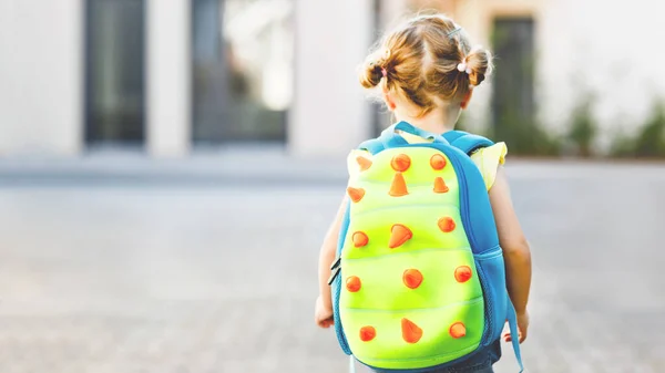 彼女の最初の日にかわいいかわいい幼児の女の子は学校に行く。保育園や幼稚園まで歩く健康な美しい赤ちゃん。バックパック付きの幸せな子供、認識できない顔. — ストック写真