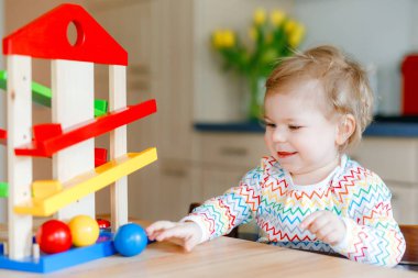 Küçük kız evde ya da çocuk odasında eğitici oyuncaklarla oynuyor. Mutlu sağlıklı çocuk renkli tahta top pisti ile eğleniyor. Çocuk top tutmayı ve yuvarlanmayı öğreniyor. Motorik eğitim.