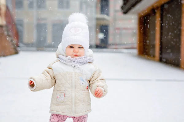 Lycklig liten flicka gör första stegen utomhus på vintern genom snö. Söta småbarn som lär sig gå. Barn har kul på kall snöig dag. Babys första snö, aktivitet. Vinterpromenad utomhus — Stockfoto