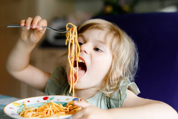 Schattig kleuter meisje eet pasta spaghetti met tomaat bolognese met gehakt vlees. Gelukkige kleuter die vers gekookte gezonde maaltijd eet met noedels en groenten thuis, binnen. — Stockfoto