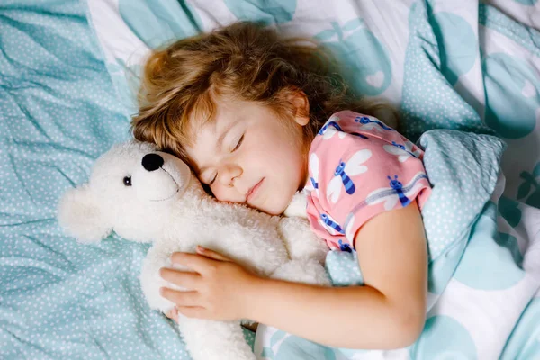 Cute little toddler girl sleeping in bed with favourite soft plush toy teddy bear. Adorable baby child dreaming, healthy sleep of children by day. Deep sleeping of toddler. Kids resting. — Stock Photo, Image