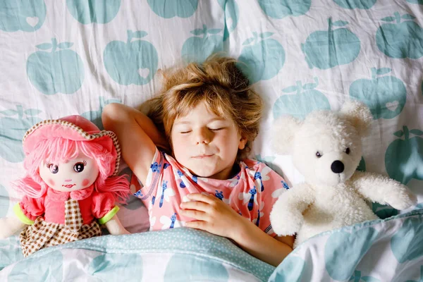 Χαριτωμένο κοριτσάκι κοιμάται στο κρεβάτι με το αγαπημένο μαλακό βελούδινα κούκλα παιχνίδι και αρκουδάκι. Αξιολάτρευτο παιδί που ονειρεύεται, υγιή ύπνο παιδιών τη μέρα. Βαθύς ύπνος νηπίου. Τα παιδιά ξεκουράζονται. — Φωτογραφία Αρχείου