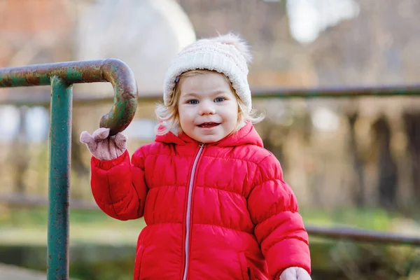 Cute toddler girl having fun on playground. Happy healthy little child climbing, swinging and sliding on different equipment. On cold day in colorful clothes. Active outdoors game for children — Stock Photo, Image