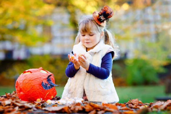 Niña pequeña vestida como un truco de bruja o trato en Halloween. Niño feliz al aire libre, con sombrero divertido naranja y bolsa de calabaza para dulce refugio. Temporada de festivales familiares en octubre. Actividades al aire libre —  Fotos de Stock