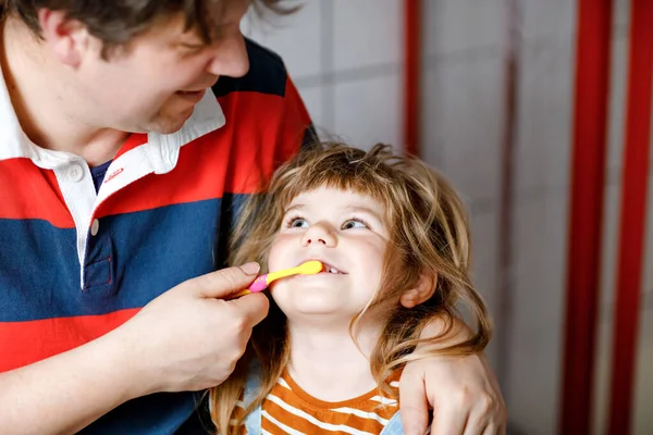 O pai a ajudar a filha a escovar os dentes. Pequena menina e pai na casa de banho, fazendo ações de higiene. Família feliz, homem e criança. Rotina matinal com crianças. — Fotografia de Stock