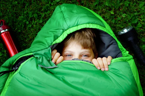 Kleuterschooljongen in slaapzak kamperen. Buitenactiviteiten met kinderen in de zomer. Plezier- en avonturenkamp, familie en vrienden vakantie of weekendje weg. Portret van kind met zaklamp. — Stockfoto