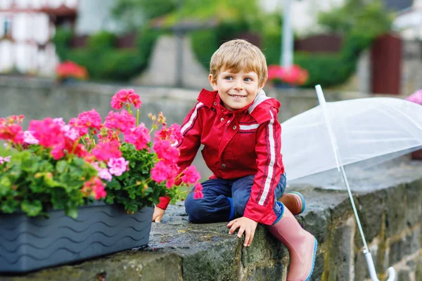 Little blond kid boy walking with big umbrella outdoors on rainy day. Portrait of cute preschool child having fun wear colorful waterproof clothes. Outdoor leisure walk on bad weather day with kids — Stock Photo, Image