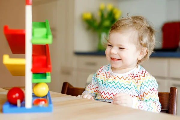 Kleine Mädchen spielen zu Hause oder im Kinderzimmer mit Lernspielzeug. Fröhliches gesundes Kleinkind, das Spaß an der bunten Kugelbahn aus Holz hat. Kind lernt Bälle zu halten und zu rollen. Motorische Bildung. — Stockfoto