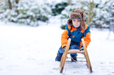 Küçük çocuk kar yağışı sırasında kızak sürmekten hoşlanıyor. Eski model kızakla gezen mutlu anaokulu çocuğu. Çocuk dışarıda karla oynuyor. Kışın aile Noel tatili için aktif eğlence