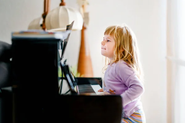 Красивая маленькая девочка играет на пианино в гостиной. Милый ребенок дошкольного возраста веселится с обучением играть на музыкальном инструменте. Раннее музыкальное образование для детей. — стоковое фото