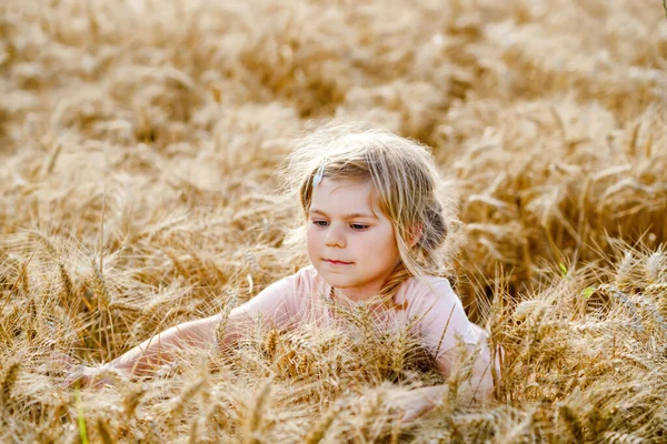 Portrait of happy smiling preschool girl in wheat grain field outdoors. Little child with blond hairs looking and smiling at the camera. Happy healthy child enjoy outdoor activity and playing. — Stock Photo, Image