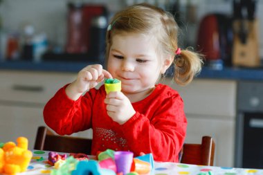 Renkli killi, sevimli, küçük bir kız. Sağlıklı bebek oyun oynuyor ve oyun hamurundan oyuncaklar yapıyor. Küçük çocuk kil kalıp ve öğrenim