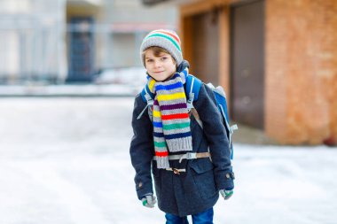 İlköğretim sınıfının küçük çocuğu kar yağarken okula yürüyor. Mutlu çocuk eğleniyor ve ilk karla oynuyor. Sırt çantalı öğrenci ya da renkli kış kıyafetleri içinde bir çanta..