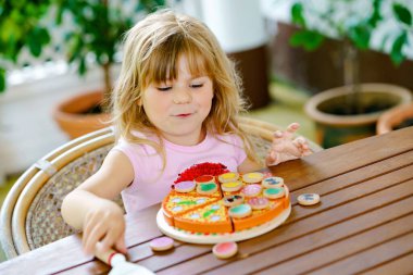 Küçük tatlı kız tahta oyuncak pizzayla oynuyor. Anaokulu çocuğu çocuklarla eğleniyor, yemekle oynamak gibi, evde oynamak gibi..