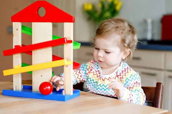 Pequena menina brincando com brinquedos educativos em casa ou berçário. Criança infantil saudável feliz se divertindo com pista de bola de brinquedo de madeira colorida. Criança aprendendo a segurar e rolar bolas. Ensino motorizado. — Fotografia de Stock