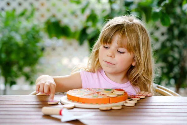 Pequena menina bonita brincando com pizza de brinquedo de madeira. Criança pré-escolar se divertindo com as crianças atividade como, brincar com alimentos, dentro de casa. — Fotografia de Stock