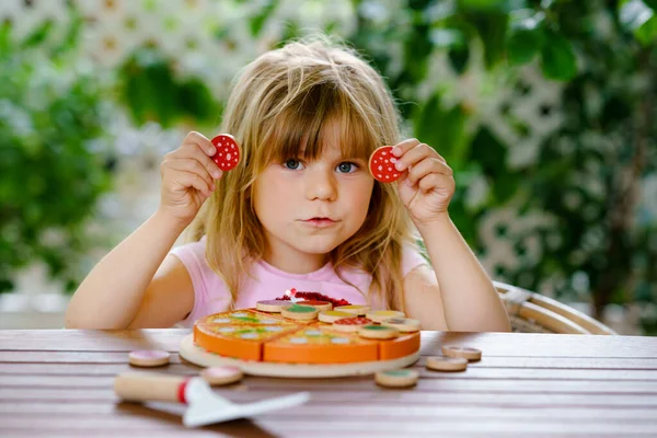 Little cute girl playing with wooden toy pizza. Preschool child having fun with children activity like, play with food, indoors. — Stock Photo, Image