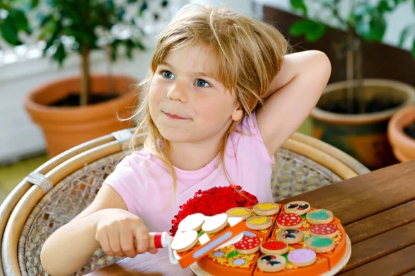 Lilla söta flicka leker med trä leksak pizza. Förskolebarn som roar sig med barnaktiviteter som, lek med mat, inomhus. — Stockfoto