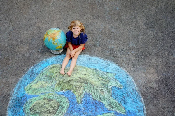 Κοριτσάκι προσχολικής ηλικίας με γήινη ζωγραφική με πολύχρωμες κιμωλίες στο έδαφος. Θετικό παιδί. Καλή ιδέα για την Ημέρα της Γης. Δημιουργία παιδιών για τη διάσωση του κόσμου, του περιβάλλοντος και της οικολογίας. — Φωτογραφία Αρχείου