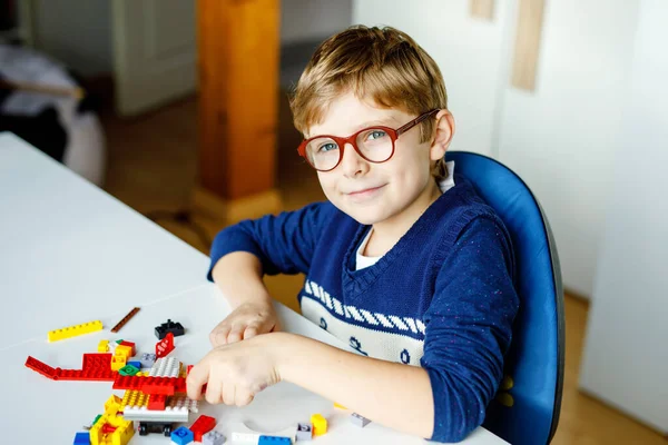 Petit enfant blond avec des lunettes jouant avec beaucoup de blocs en plastique coloré. Adorable écolier qui s'amuse avec la construction et la création de robots. Loisirs créatifs technique moderne et robotique. — Photo