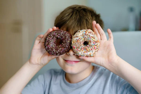 Menino da escola pré-adolescente feliz comendo donut doce em casa. Criança loira na cozinha doméstica ou na cantina da escola Criança bonito e comida açucarada insalubre. — Fotografia de Stock