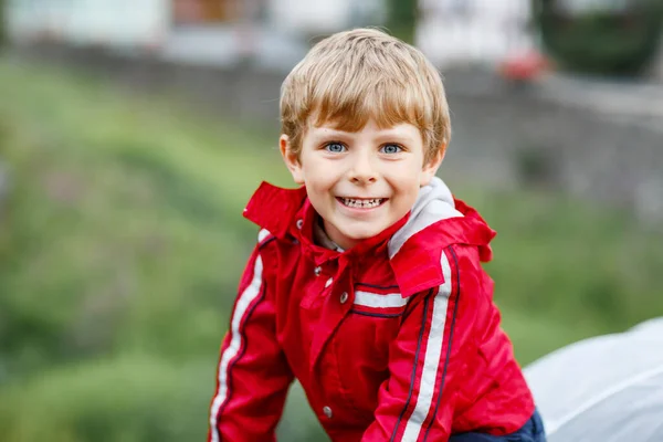 Liten blond pojke som går utomhus på regnig dag. Porträtt av söta förskolebarn som har kul bära färgglada vattentäta kläder. Fritid utomhus promenad på dåligt väder dag med barn. — Stockfoto