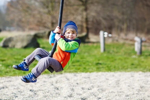 Pequeño niño sonriente de dos años divirtiéndose en swing en día frío — Foto de Stock