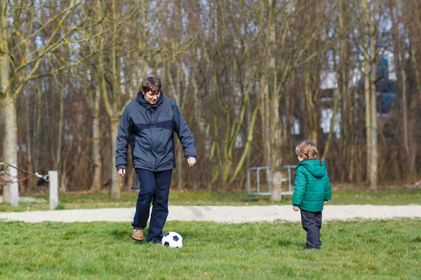 Padre joven con su pequeño hijo jugando al fútbol en el patio de recreo . —  Fotos de Stock