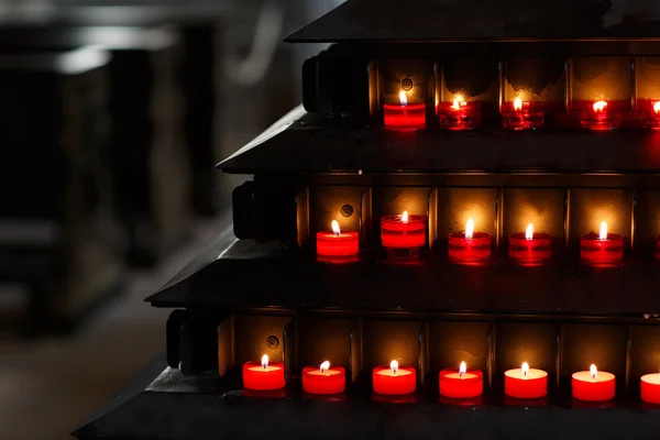 Große Gruppe brennender Kerzen vor schwarzem Hintergrund in der Kirche — Stockfoto