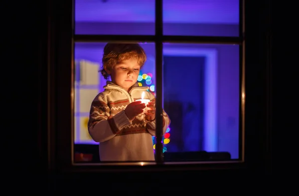 Niedliches Kleinkind steht zur Weihnachtszeit am Fenster und hält — Stockfoto