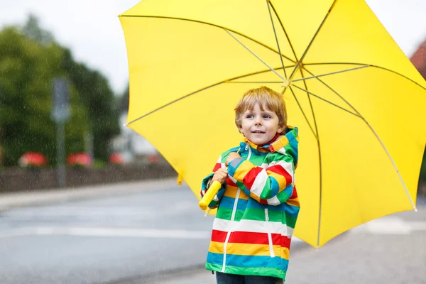 可爱的蹒跚学步的男孩，把黄色的雨伞和五彩缤纷的夹克 ou — 图库照片