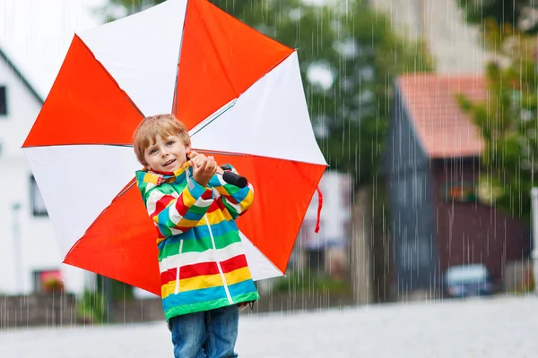 Lachende jongen met gele paraplu en kleurrijke jas buitenshuis op — Stockfoto