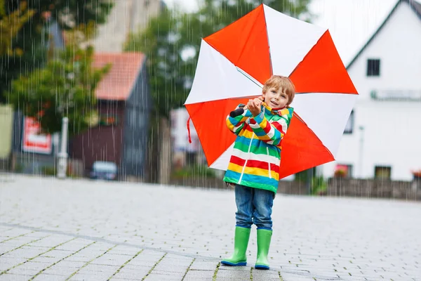 Smiling boy with yellow umbrella and colorful jacket outdoors at — Stock Photo, Image