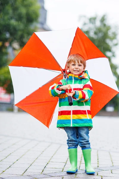 Menino bonito com guarda-chuva amarelo e jaqueta colorida ao ar livre — Fotografia de Stock