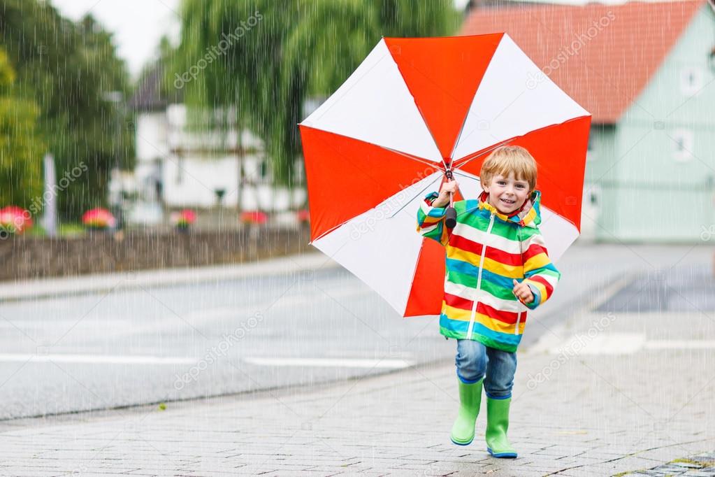 Beautiful child with red umbrella and colorful jacket outdoors a