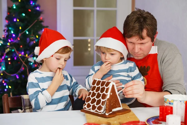 Vater und zwei kleine Söhne beim Zubereiten eines Lebkuchenhauses — Stockfoto