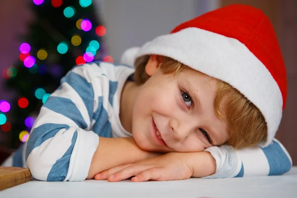 Kleine jongen in Kerstman hoed met kerstboom en verlichting — Stockfoto