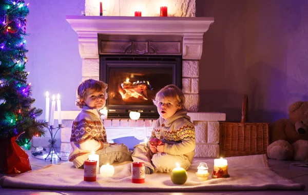 Due bambini piccoli seduti accanto a un camino a casa a Natale — Foto Stock