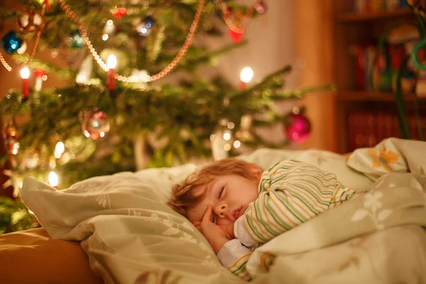 Küçük şirin sarışın çocuk Noel ağacının altında uyuyor — Stok fotoğraf