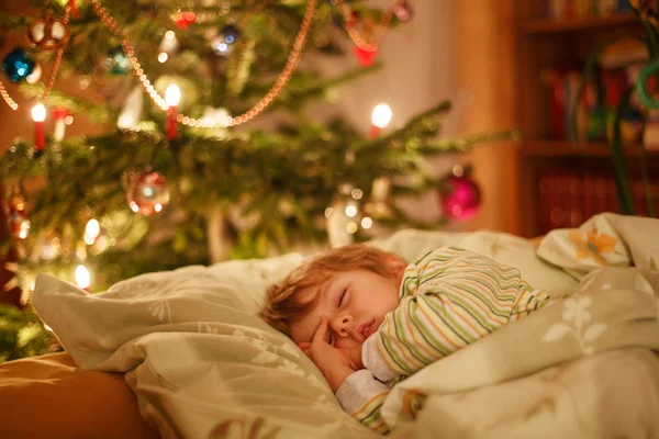 Pequeño niño rubio lindo durmiendo bajo el árbol de Navidad — Foto de Stock