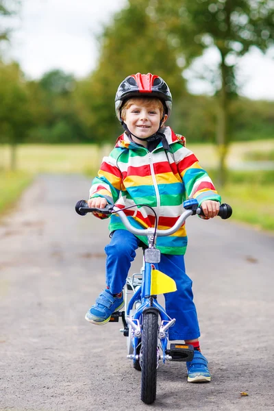 Adorable niño en casco rojo y colorido impermeable montado en su — Foto de Stock