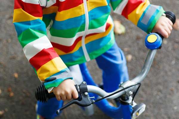 Criança em capa de chuva colorida montando sua primeira bicicleta — Fotografia de Stock